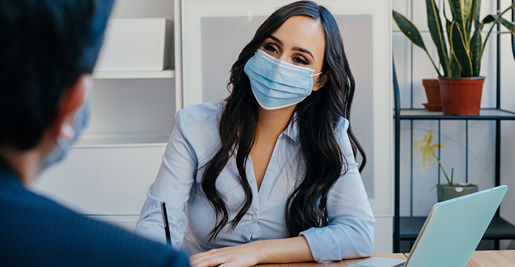 Everlytic | Blog | Launch Your Next Product or Service with the Sideways Sales Letter | Blog Image | Two Professionals Looking at Each Other In the Office with Masks on While social Distancing