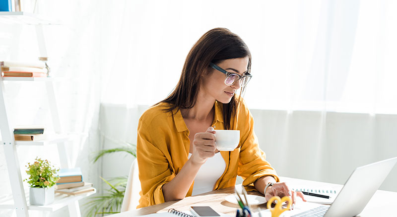 Everlytic | Blog | 5 Good Reasons to Use Email Marketing for Your Retail Store | Caucasian Woman with White Tea Cup on the Hand | Using a Laptop | Blog Image