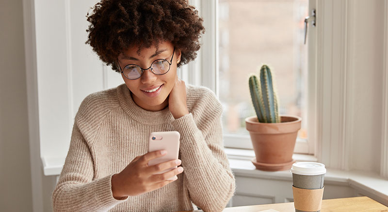 Everlytic | Blog | 5 Good Reasons to Use Email Marketing for Your Retail Store | Young African Woman with Natural Hair | Using Mobile Device | Blog Image